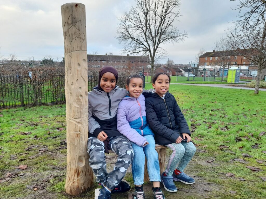 three children sit on a carved bench