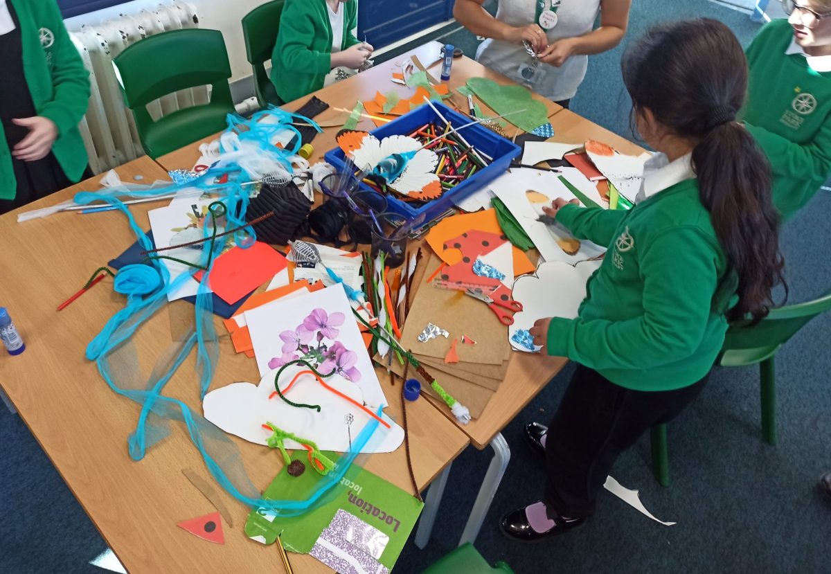 A child at a messy table of art materials and recycled items