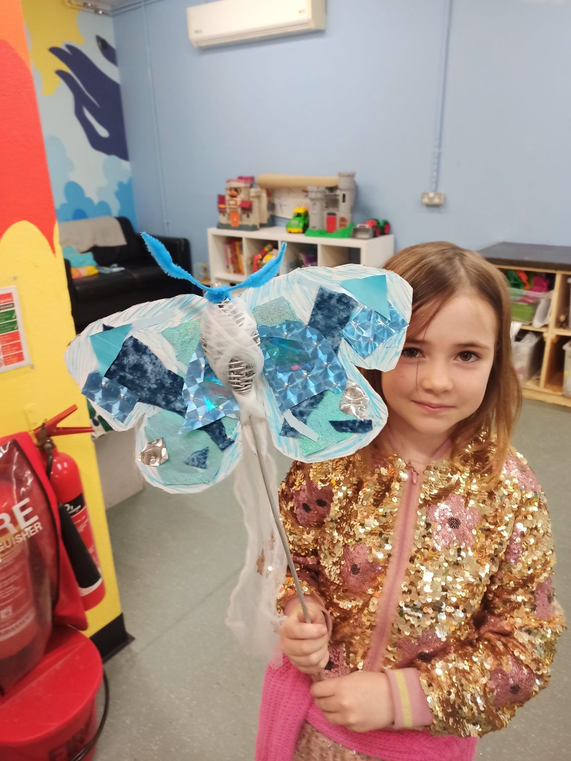 A child holding up a decorated paper butterfly