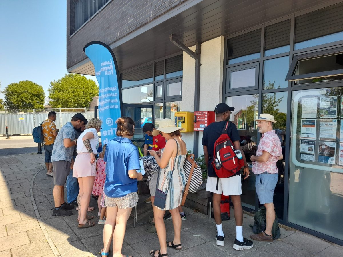 People gather in the shade outside the Hub, in bright sunlight.