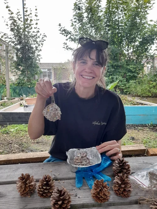 A white woman holds up a pine cone with fat and seeds in the gaps