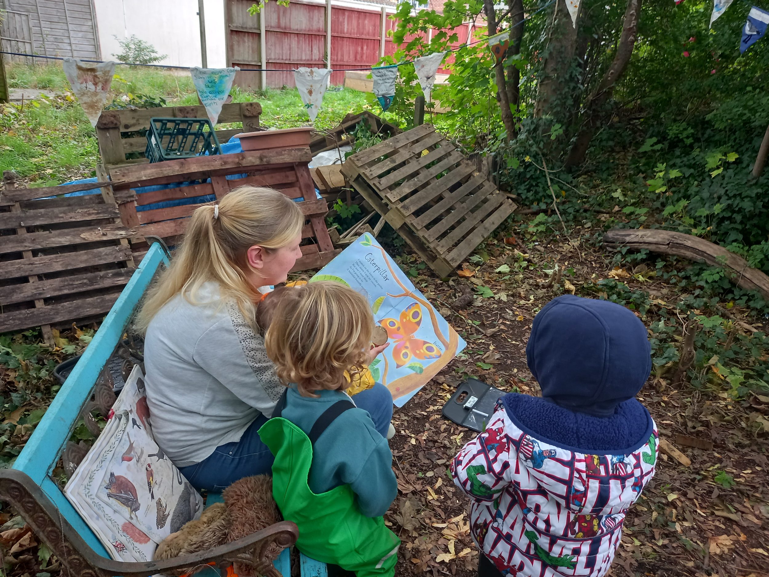 two small children read a book outdoors with an adult