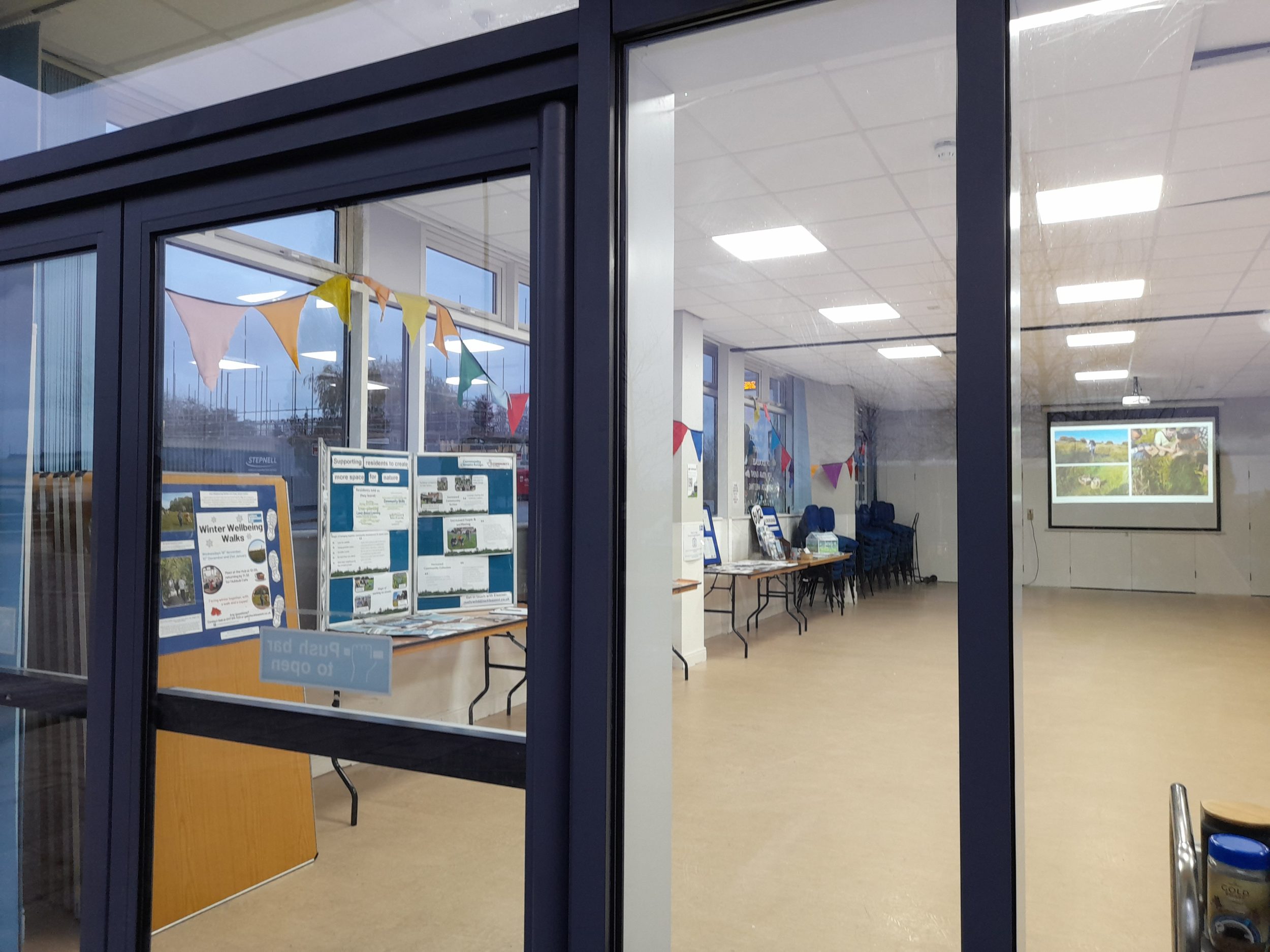 image of the Hub taken from outside with bunting, display stands and photos of people doing garden work projected onto the back wall
