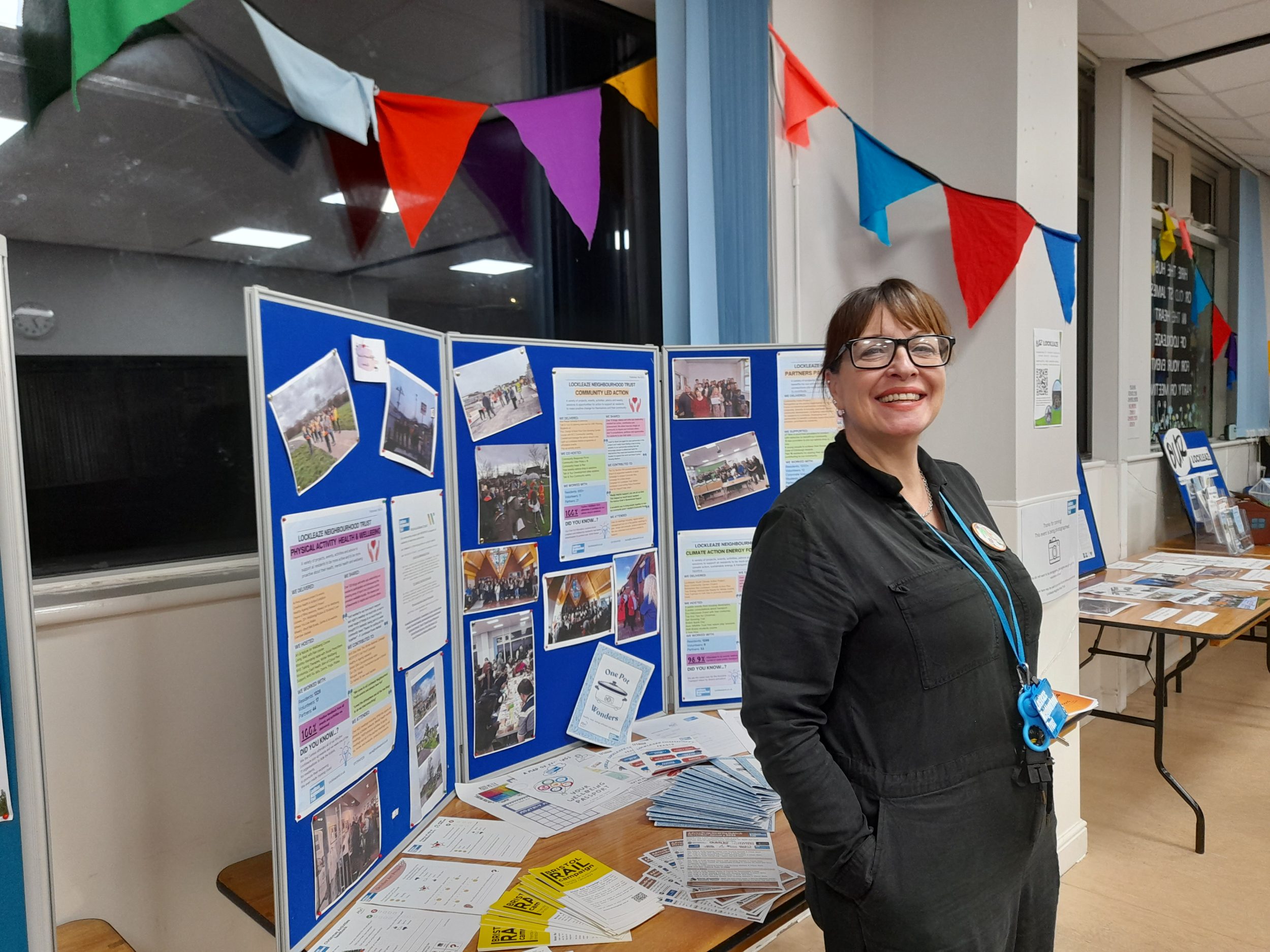 A woman in black jumpsuit and LNT lanyard smiles proudly in front of a display board
