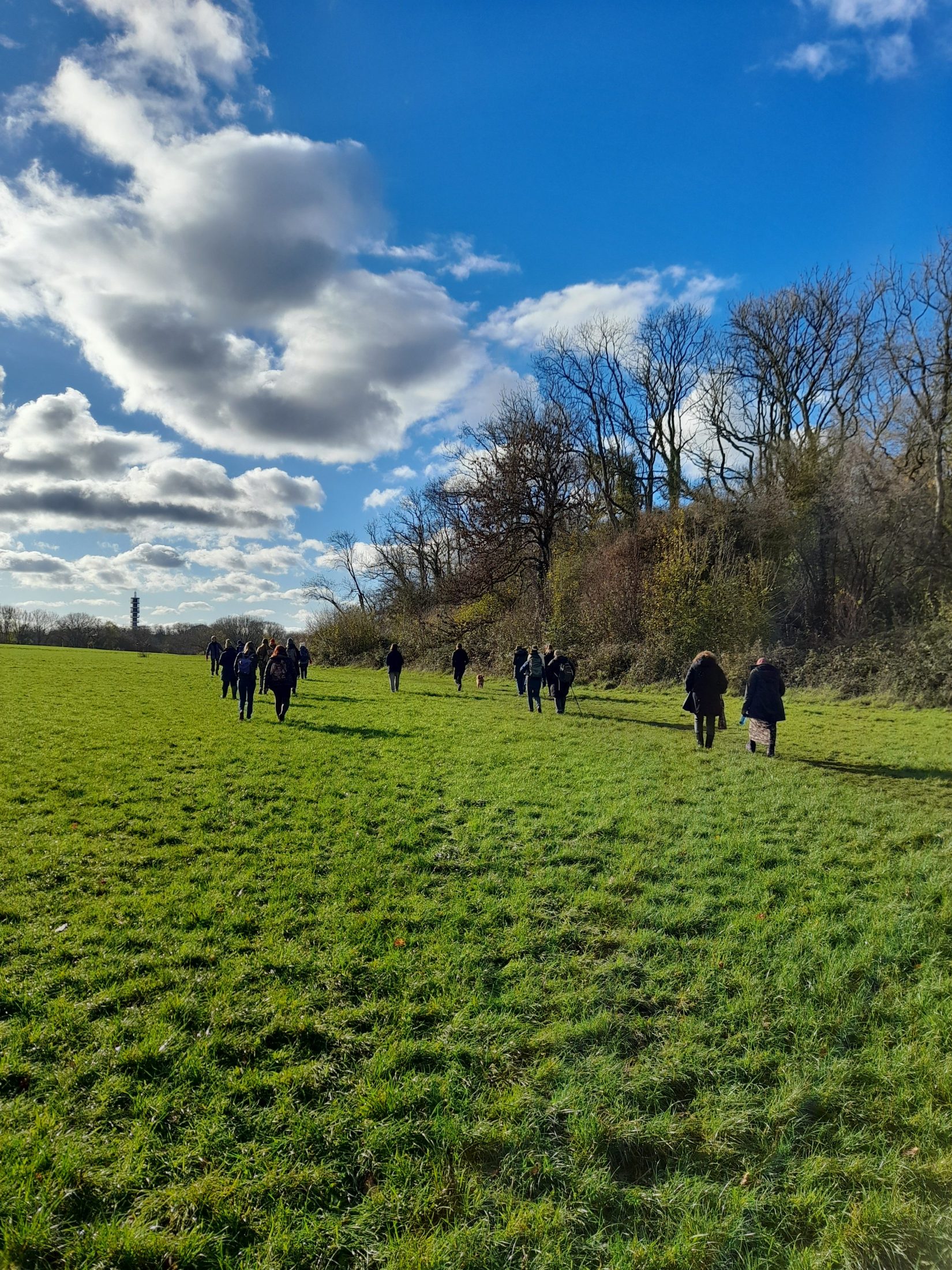 walkers in the distance walk along a field. the purdown tower is in the distance.