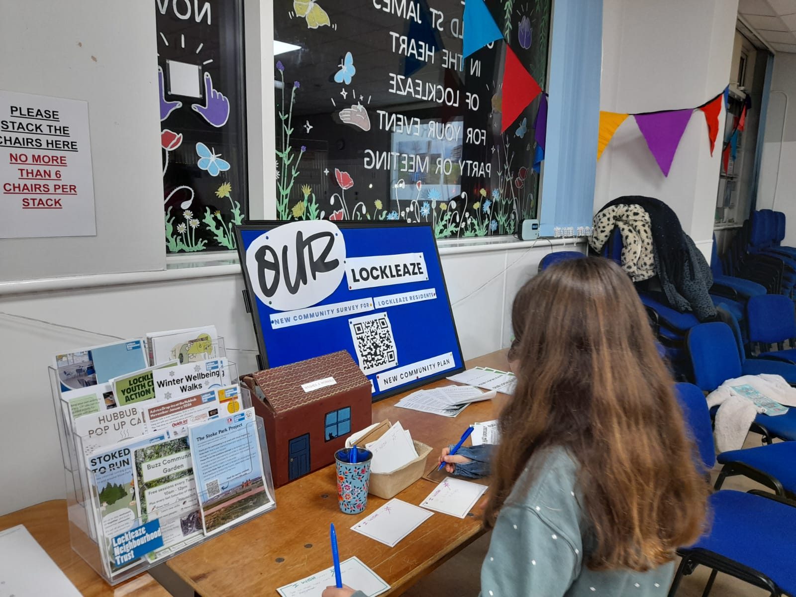 a young girl has her back to us while writing on a card at a stand labelled 'our lockleaze, the new community plan survey