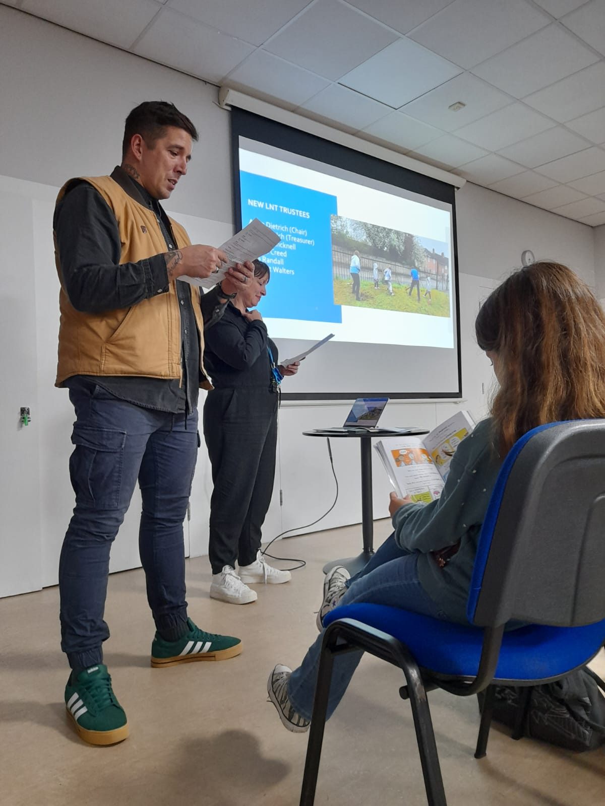 two people present from a slideshow, with a child reading a book in the foreground