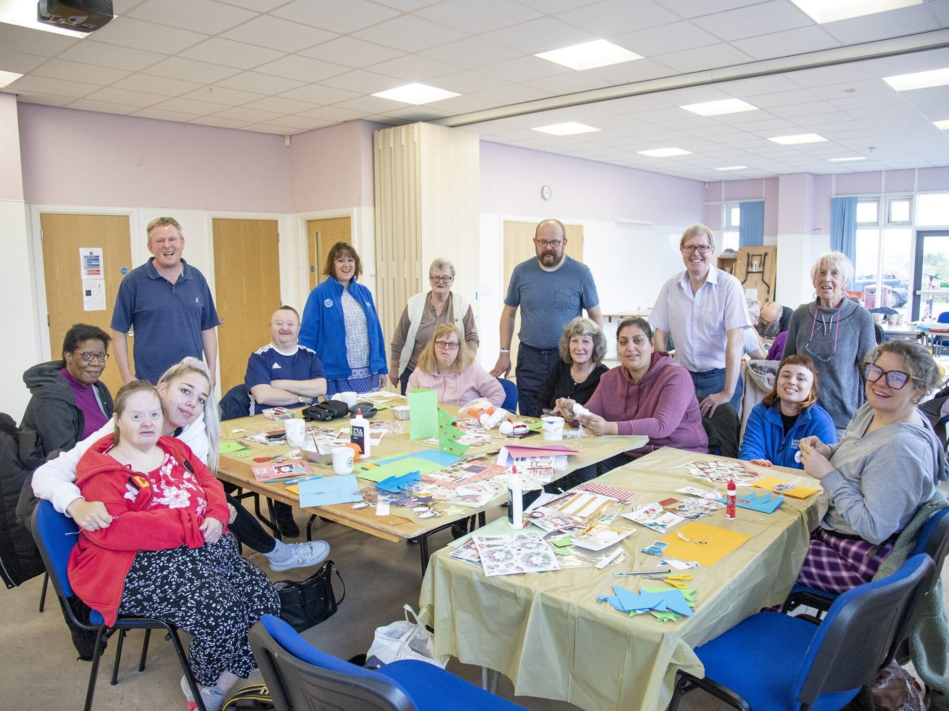 Thirteen people, some of whom have disabilities, around a table with lots of art supplies