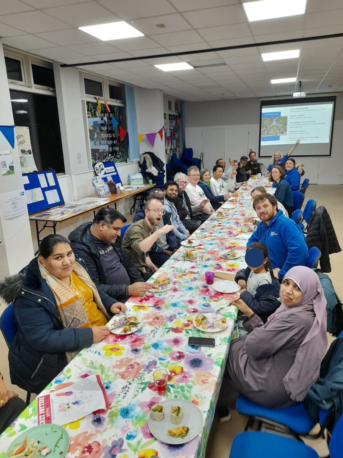 about 20 people on both sides of along table with food smile a the camera