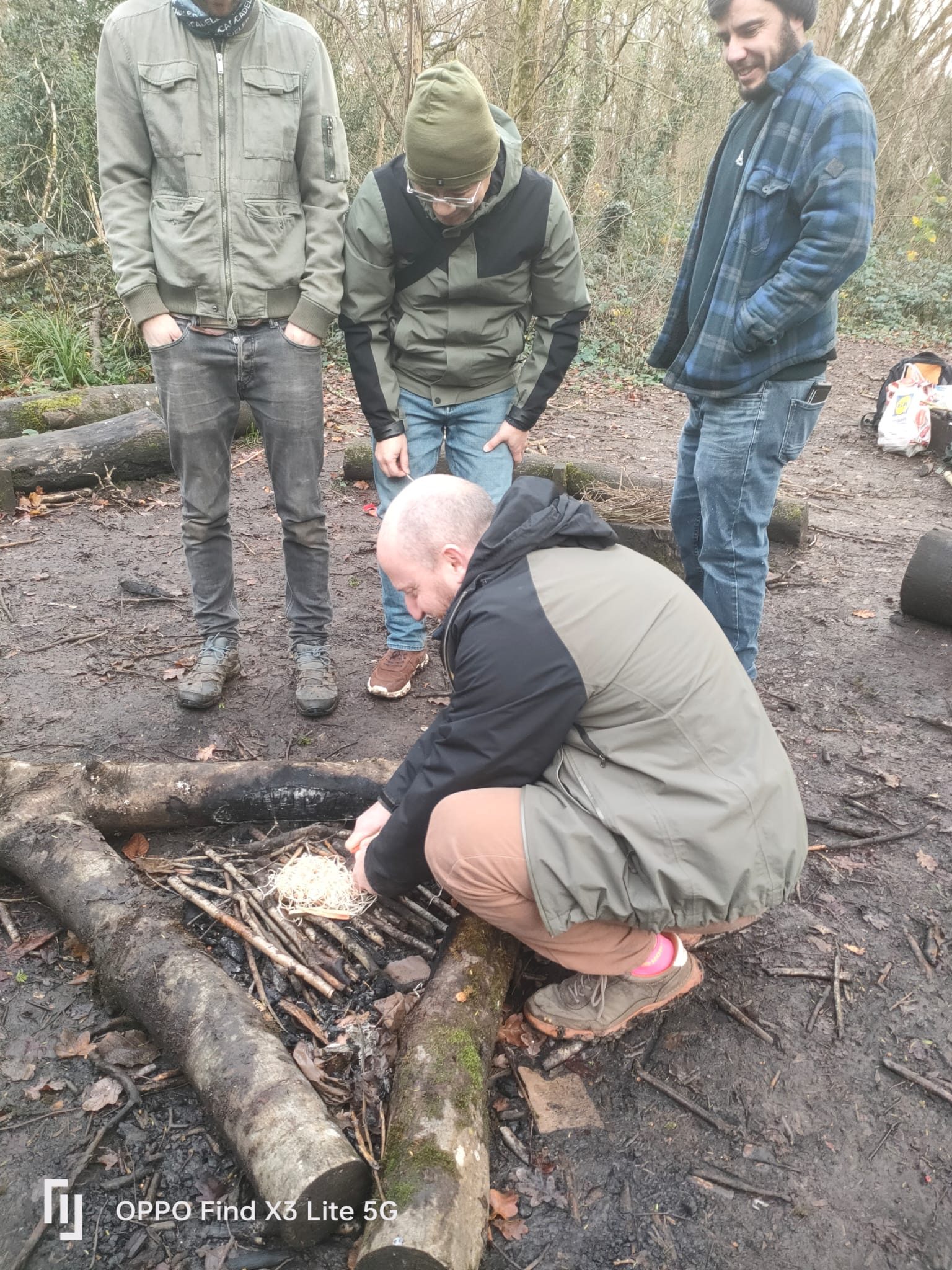 a man builds a fire, positioning a pile of smaller sticks witihin a boundary made by three larger logs