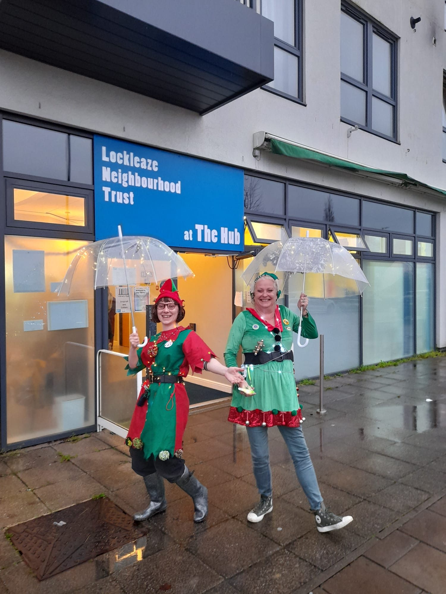 two women dressed as elves with lit up umbrellas smile outside The Hub