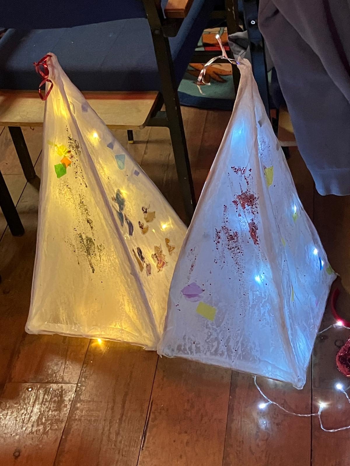 two triangular lanterns made with paper and willow lit from inside