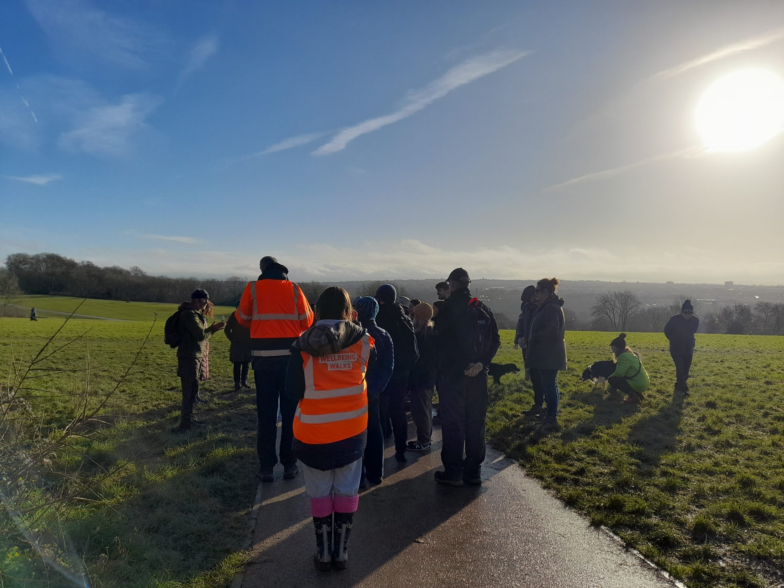 a cluster of people on a paved path through a field with a wide view. two wear orange hi vis.