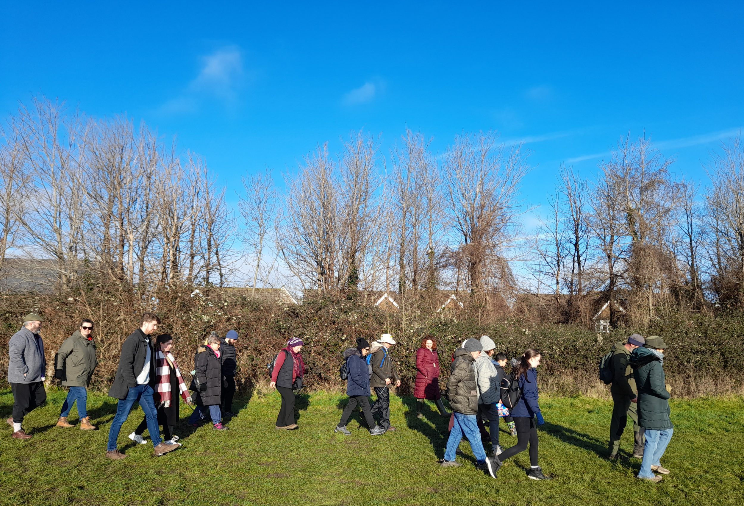 about twenty people march across a field bordered by trees