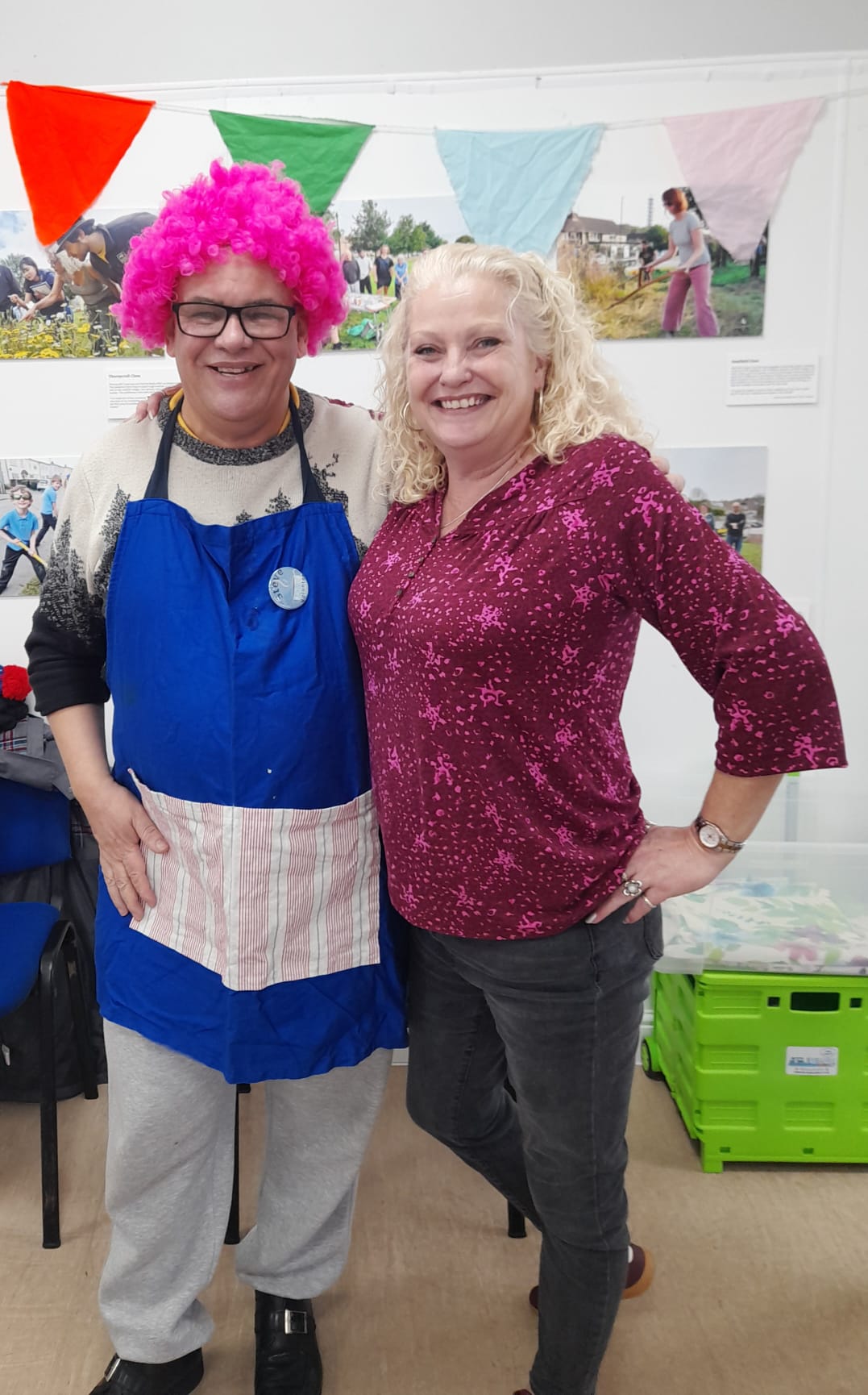 a man in an apron and a curly pink wig and a woman smile