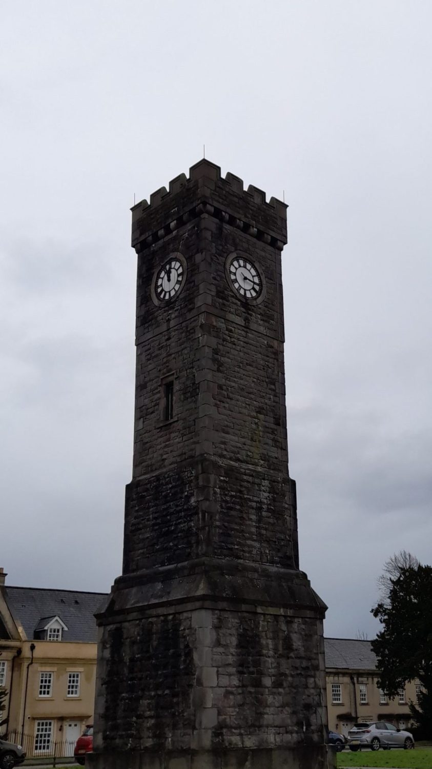 a tall, crenellated tower made of dark stone with clocks set into the top on both sides