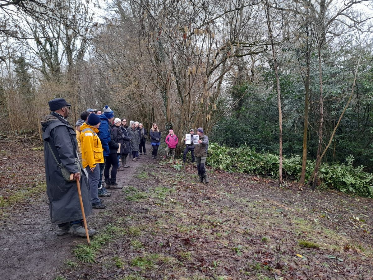 a group of walkers along a path looking down at two presenters holding up photos