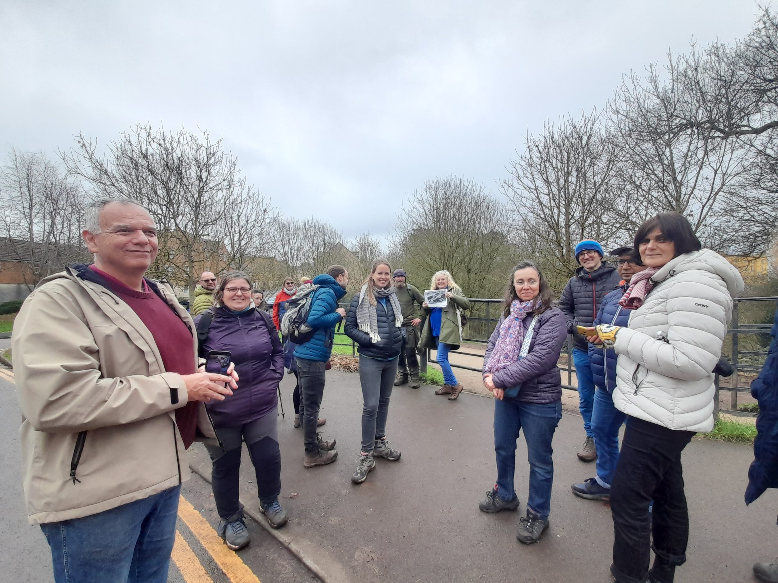 a mixed age group smile standing on a path. there are bare trees and blue sky