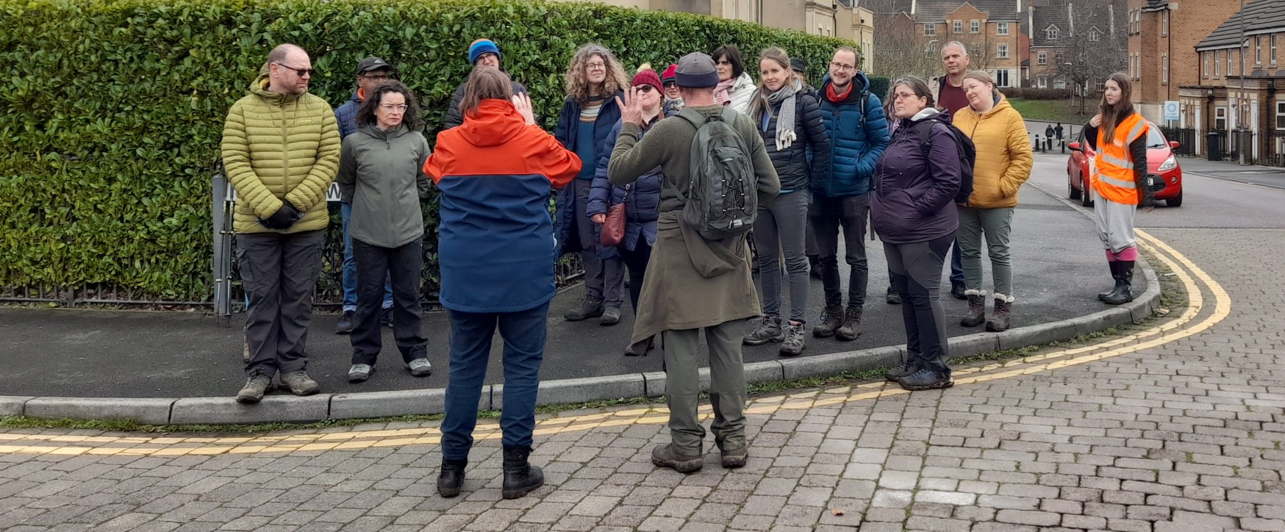 A group of walkers face two people, both of whom hold up their hands with four fingers- steve and a BSL interpreter