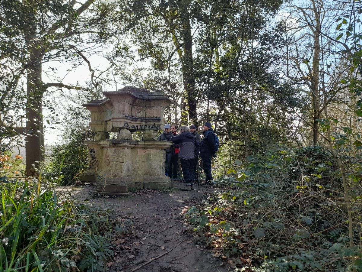 walkers in a woody glade with a stone monument