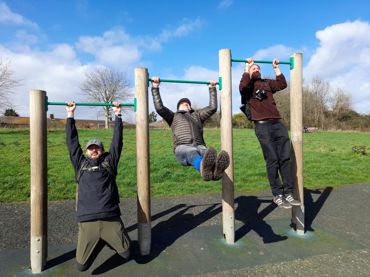 three men handing from horizontal exercise bars, ascending in height