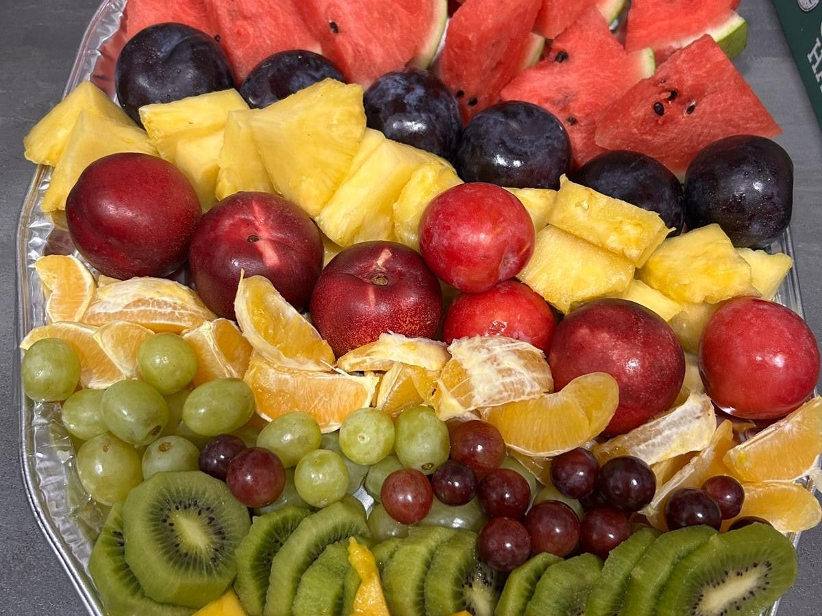 a plate with sliced kiwi, grapes, orange slices, plums, sliced pineapple and watermelon