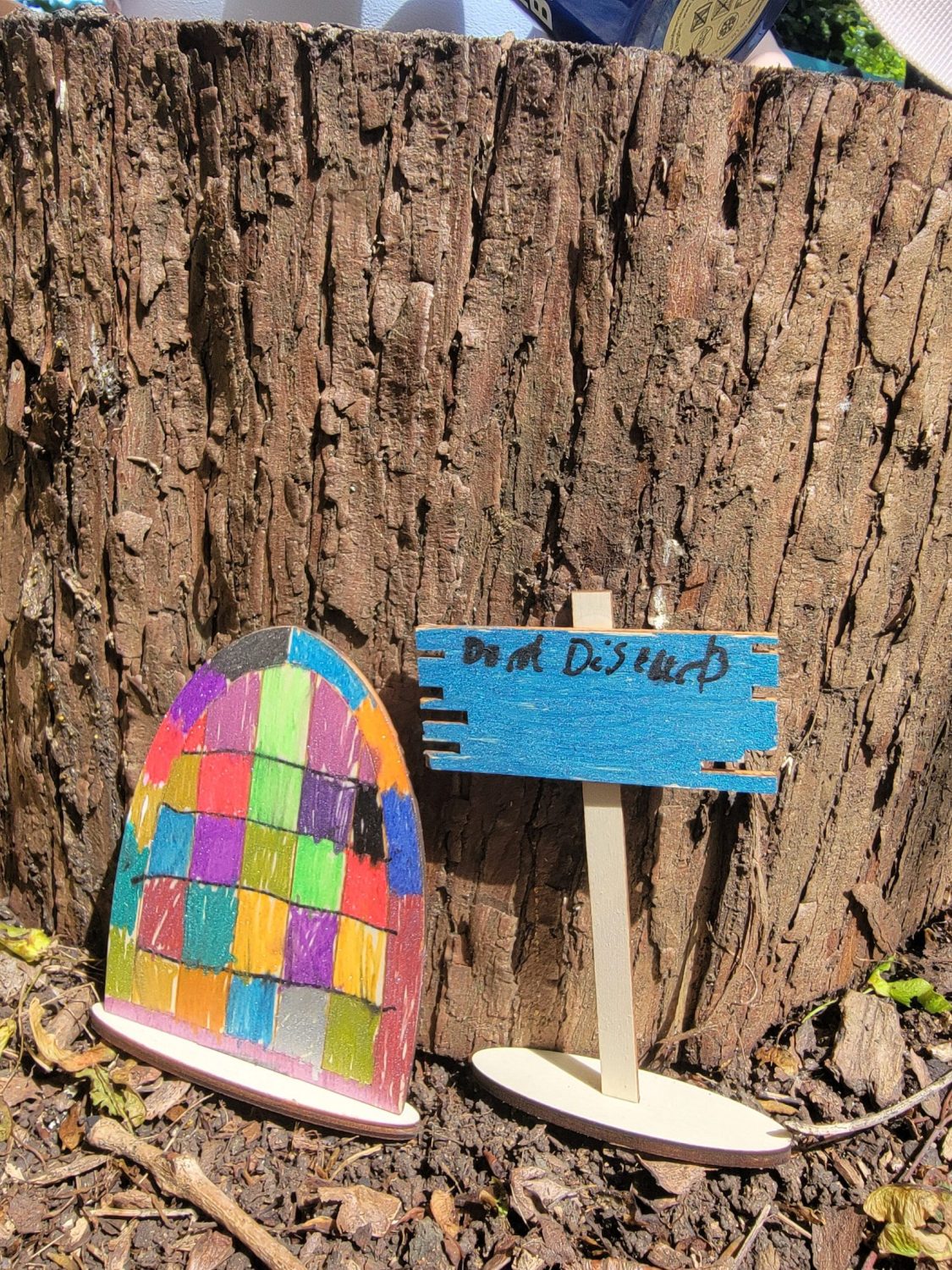 a little wooden door and sign saying do not disturb, drawn by a child and placed against a tree stump