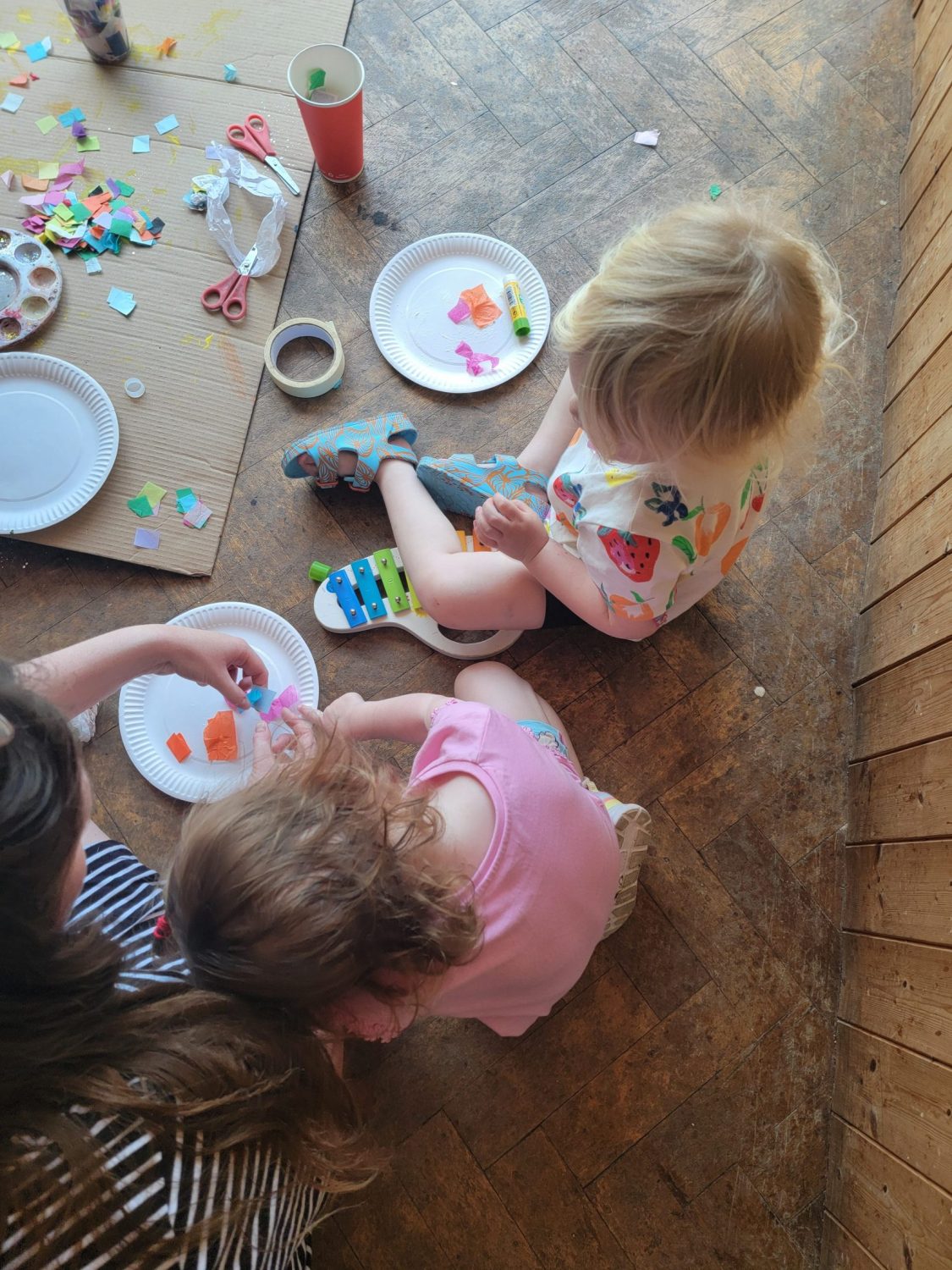 two children sit on the floor amongst art materials