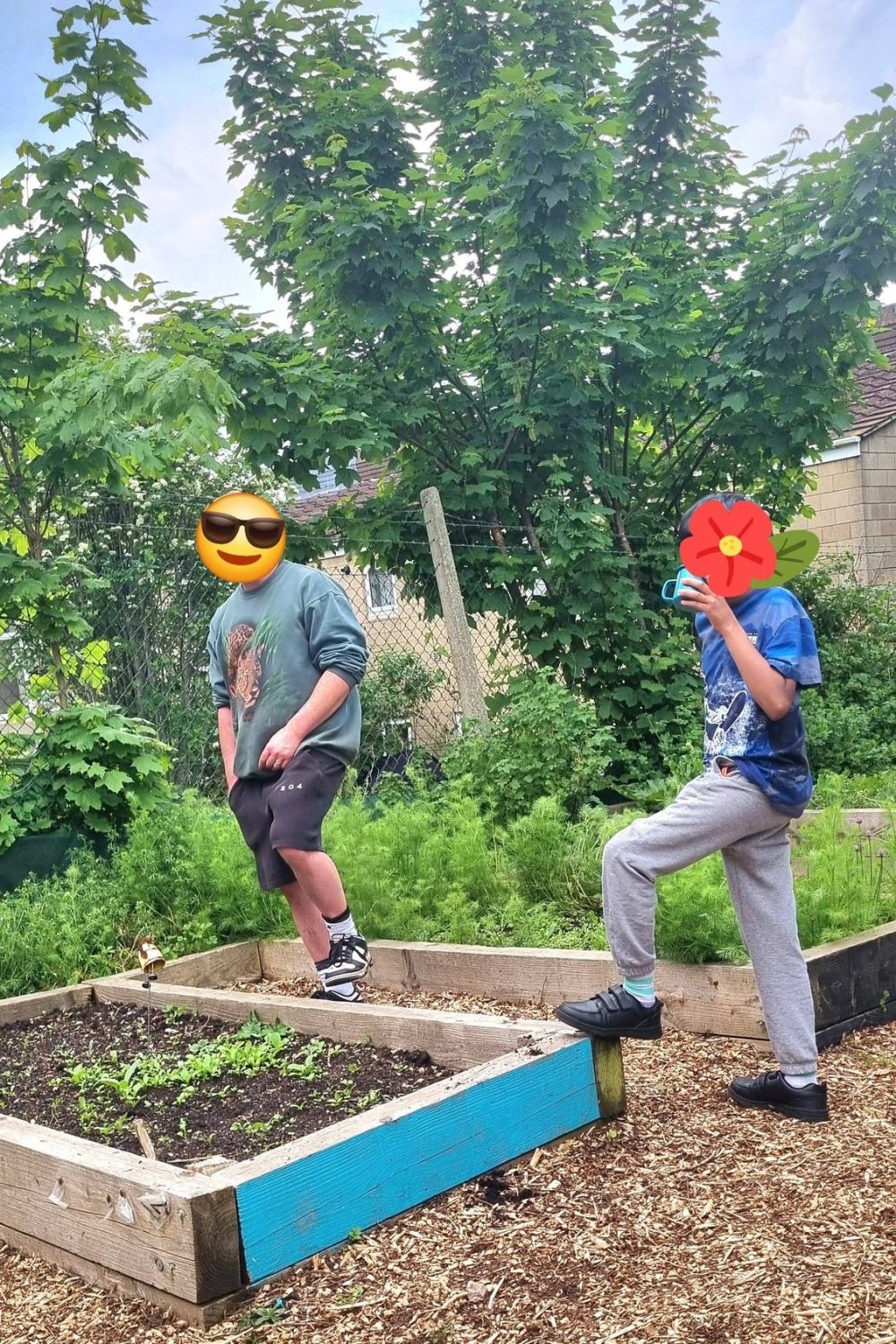 two young volunteers with their faces covered by flower and shades emojis pose by flowerbeds