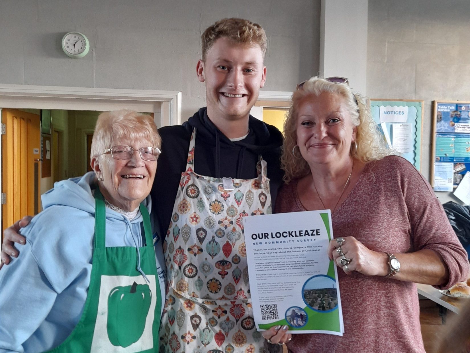 A woman, older lady and young man wearing aprons hold up a copy of the community survey in a church.