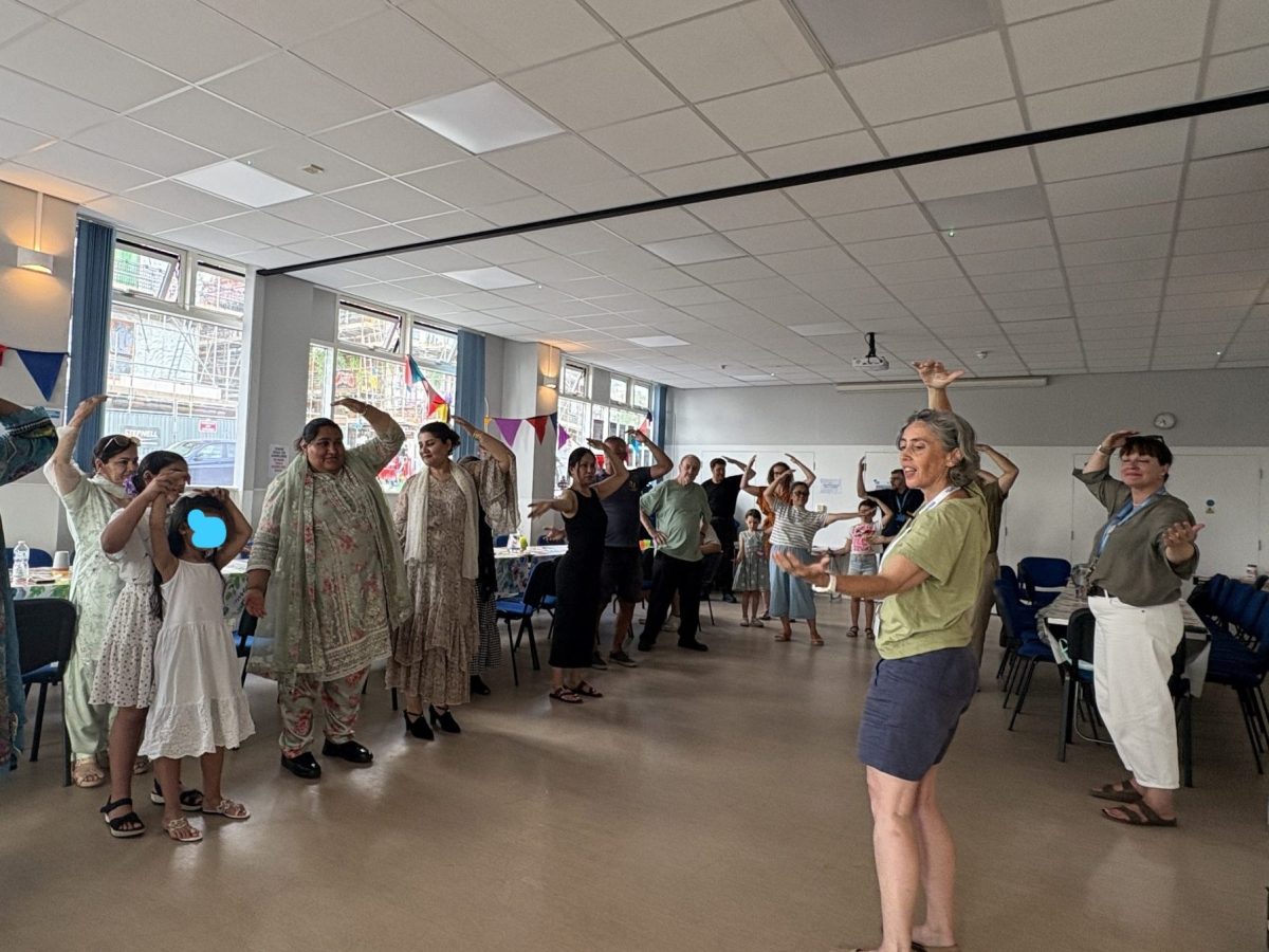 families raise their hands in a tai chi pose in the Hub with Cat, and older woman leading in the front