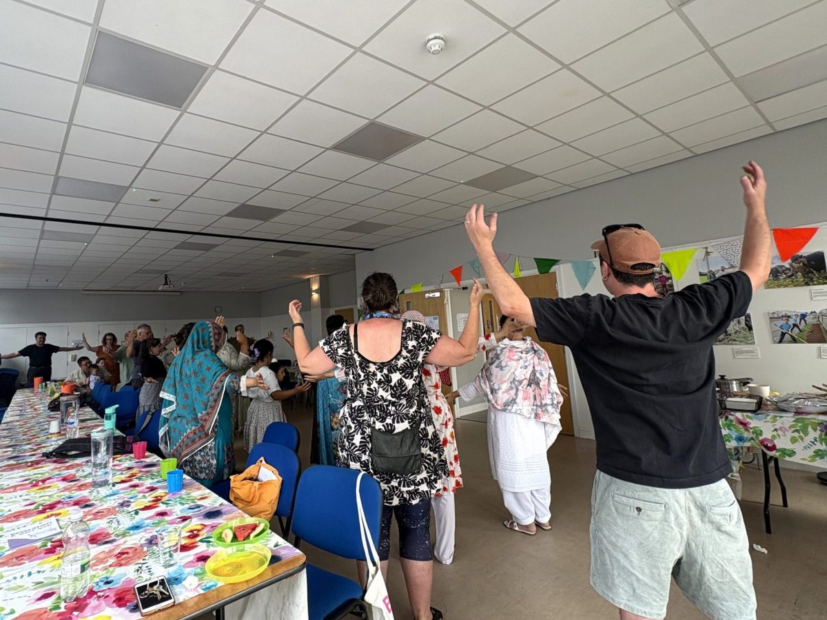 lots of people raise their hands in a tai chi pose. to the left is a long table with colourful cloth and cups