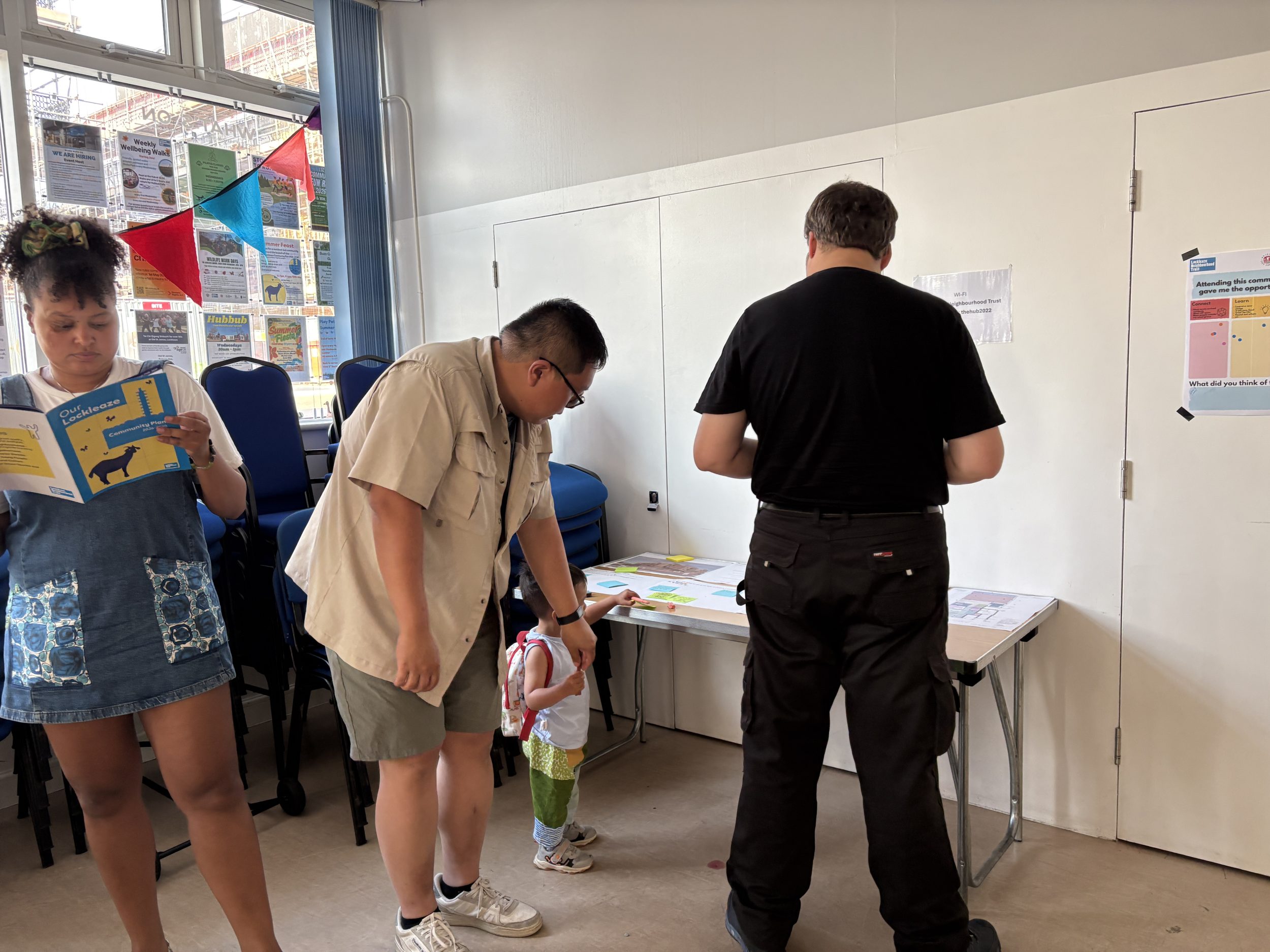 two men and a little boy look at a table with pages. a woman reads the our lockleaze community plan 2026-2030