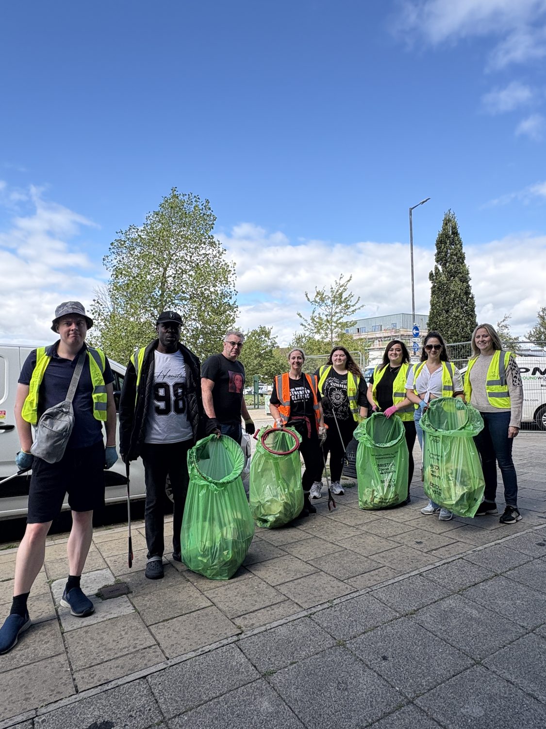 eight people stand on the square with full green bags of litter and hi vis jackets